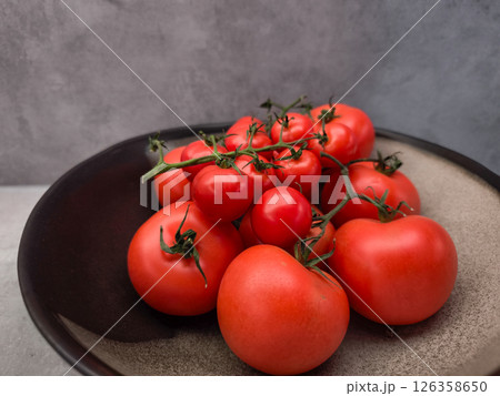 Ripe red tomatoes and cherry tomatoes on the vine, presented on a dark plate, creating a vibrant display of freshness Ripe red tomatoes and cherry tomatoes on the vine, presented on a dark plate, creating a vibrant display of freshness 126358650