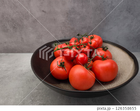 Ripe red tomatoes clustered on vine, resting in black ceramic bowl, showcasing garden fresh produce background wallpaper copy space Ripe red tomatoes clustered on vine, resting in black ceramic bowl, showcasing garden fresh produce background wallpaper copy space 126358655