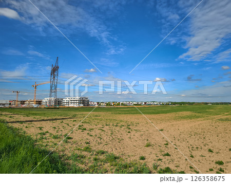 Power lines crossing a field near a construction site under blue sky 126358675