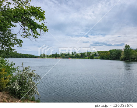 Lake reflecting cloudy sky with lush green trees Hostivar Dam Beach in Prague 126358676