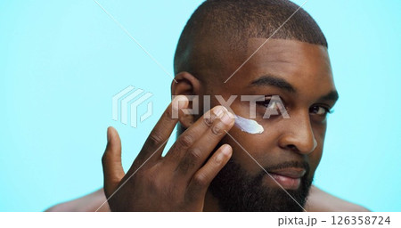 Portrait, cream and black man in studio, cosmetics and dermatology on blue background. African person, space and model with shine, creme and lotion with skincare, aesthetic and facial spf with glow 126358724