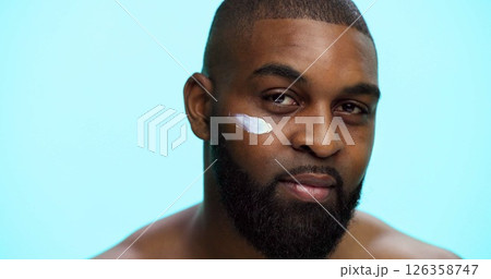 Portrait, cream and black man with cosmetics, skincare and dermatology on blue studio background. African person, space and model with shine, creme and glow with moisturiser, beauty and facial spf Portrait, cream and black man with cosmetics, skincare and dermatology on blue studio background. African person, space and model with shine, creme and glow with moisturiser, beauty and facial spf 126358747
