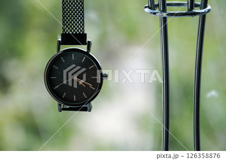 A close-up of a minimalist wristwatch in a plant-filled room, showcasing its design and the softness of natural light filtering through 126358876