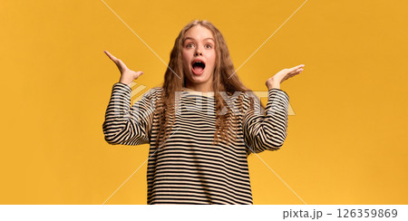 Young woman expressing surprise and shock with her mouth open and hands raised in gesture of disbelief against yellow studio background. Young woman expressing surprise and shock with her mouth open and hands raised in gesture of disbelief against yellow studio background. 126359869