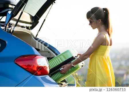 Young woman taking green suitcase from car trunk. Travel and vacations concept. Young woman taking green suitcase from car trunk. Travel and vacations concept. 126360733
