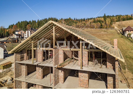 Wooden frame of new roof on a brick big house under construction. 126360781