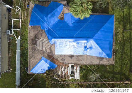 Top view of leaking house roof covered with protective tarp sheets against rain water leaks until replacement of asphalt shingles. Damage of building rooftop as aftermath of hurricane Ian in Florida 126361147