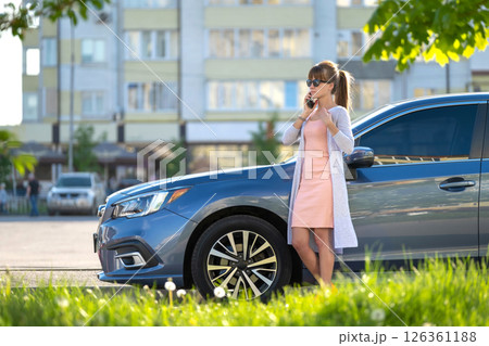 Stylish woman driver standing near her vehicle talking on cellphone on city street in summer. Stylish woman driver standing near her vehicle talking on cellphone on city street in summer. 126361188