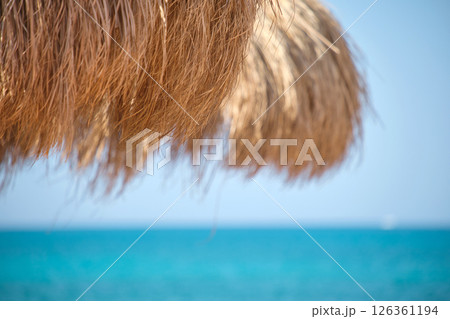 Straw shade umbrella in sea tropical region against blue vibrant sky in summer Straw shade umbrella in sea tropical region against blue vibrant sky in summer 126361194