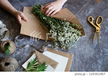 Creating a rustic floral arrangement with natural materials on a textured surface in a cozy crafting space 126361967