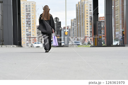 Woman crossing street with purple shopping bag in casual black outfit on a crosswalk. Woman crossing street with purple shopping bag in casual black outfit on a crosswalk. 126361970