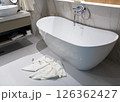 A freestanding modern bathtub with white towels left on the bathroom floor after use 126362427