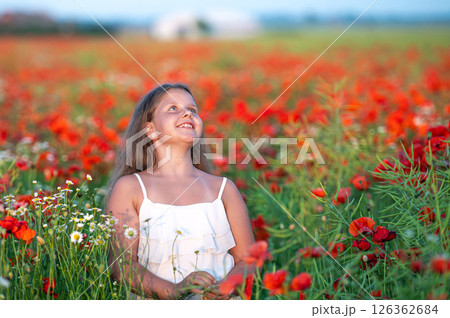 cute girl wearing white dress in summer blooming poppy field walking under evening sun 126362684