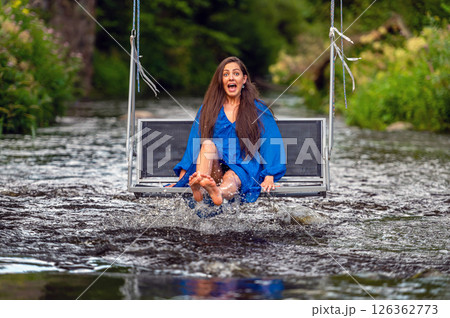 a joyful young woman swings on a rope swing across a fast-flowing river 126362773