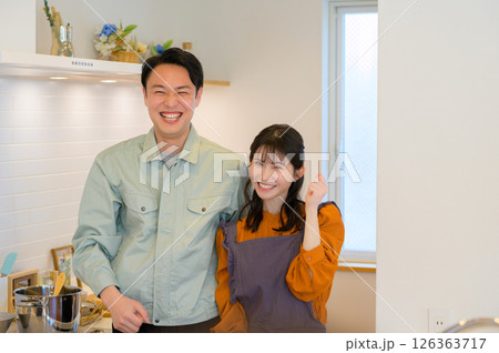 キッチンで並ぶ作業服の日本人男性と主婦の女性 キッチンで並ぶ作業服の日本人男性と主婦の女性 126363717