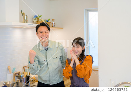 キッチンで並ぶ作業服の日本人男性と主婦の女性 キッチンで並ぶ作業服の日本人男性と主婦の女性 126363721