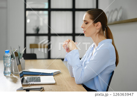 Focused woman engaging in a virtual meeting at a modern workspace during the day Focused woman engaging in a virtual meeting at a modern workspace during the day 126363947