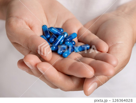 Cupped female hands with a pile of blue medical herbal capsules closeup over white shirt 126364028