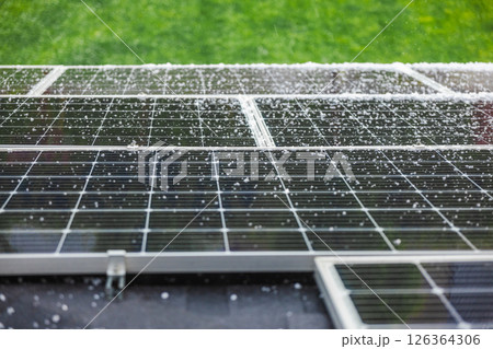 Solar panels covered with raindrops and small hailstones during a rainy day with green grass background. 126364306