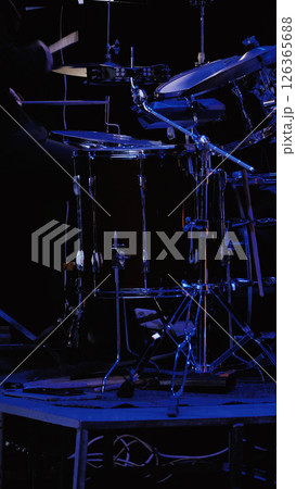 Close-up of a drum kit and a drummer behind it on a dark stage with blue lighting. The background is blurred. Close-up of a drum kit and a drummer behind it on a dark stage with blue lighting. The background is blurred. 126365688