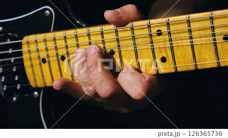 Macro shot of fingers pressing against the maple deck of an electric guitar, showing in detail the metal fret, position points and nickel strings. Macro shot of fingers pressing against the maple deck of an electric guitar, showing in detail the metal fret, position points and nickel strings. 126365736