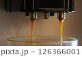 A close-up of an espresso machine with two spouts pouring espresso into a glass cup. The espresso is a dark brown color and is dripping into the cup. 126366001