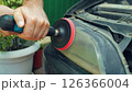 A close-up a person using a power drill with a buffing attachment to restore a cloudy and discolored car headlight. The headlight lens is being polished to improve its clarity and appearance. 126366004