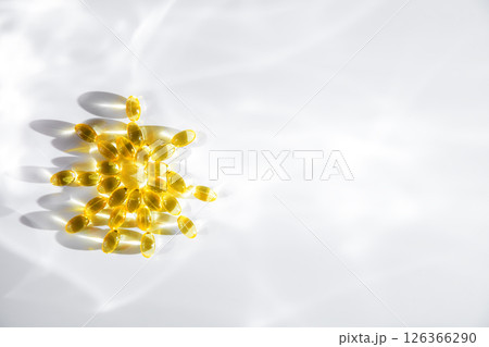 vitamin D or Fish oil yellow transparent capsules forming a sun shape on a white background, emphasizing themes of health, wellness, and nutrition 126366290