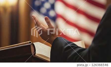 Close-Up of Speaker s Hand at Podium with Open Book and Blurred American Flag in Background 126366546