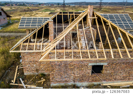 Private residential house with wooden roof frame structure under construction. Unfinished brick building under development. 126367083