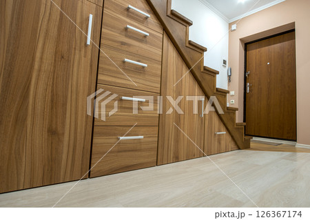 Modern architecture interior with luxury hallway with glossy wooden stairs in multi-storey house. Custom built pullout cabinets on glides in slots under stairs. Use of space for storage. 126367174
