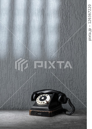 Vintage black telephone with rotary dial on gray stone table. 126367220