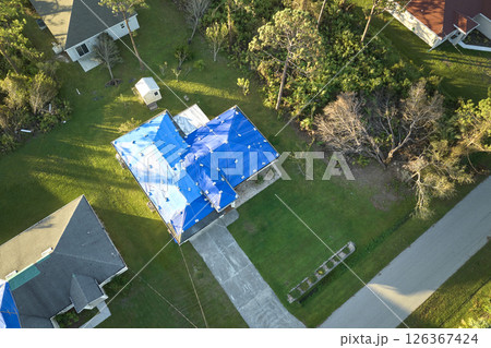 Hurricane Ian damaged house rooftops covered with protective plastic tarp against rain water leaking until replacement of asphalt shingles. Aftermath of natural disaster 126367424