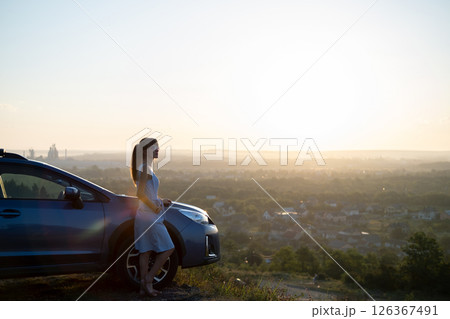 Happy young woman driver in blue dress leaning on her car enjoying warm summer day. Travelling and vacation concept. 126367491