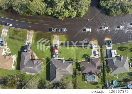 Flooded american street with moving vehicles and surrounded with water houses in Florida residential area. Consequences of hurricane natural disaster Flooded american street with moving vehicles and surrounded with water houses in Florida residential area. Consequences of hurricane natural disaster 126367573