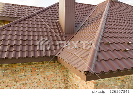 Detail of house roof structure covered with brown metal tile sheets. 126367841