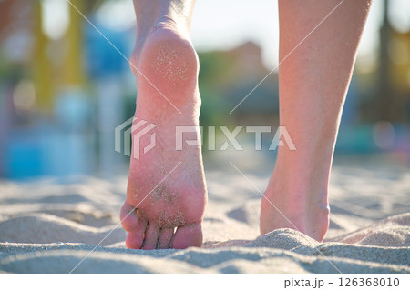 Close up of female feet walking barefoot on white grainy sand of golden beach on blue ocean water background Close up of female feet walking barefoot on white grainy sand of golden beach on blue ocean water background 126368010