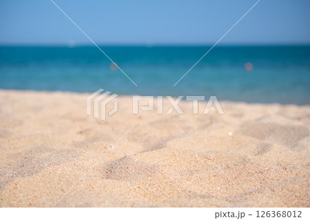 Close up of clean yellow sand surface covering seaside beach with blue sea water on background. Travel and vacations concept. 126368012