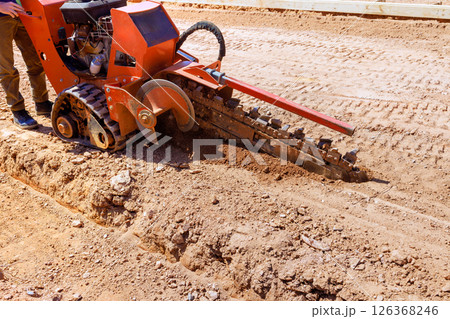 Worker uses trencher to dig seam for underground utilities at construction site. 126368246