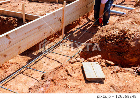 Construction worker sets up rebar wooden frames for new foundation on job site. Construction worker sets up rebar wooden frames for new foundation on job site. 126368249