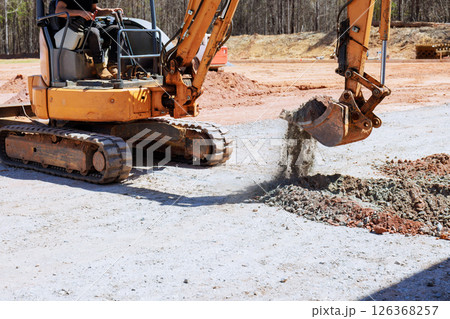 Heavy machinery operator uses an excavator to digs trench, move gravel at construction site Heavy machinery operator uses an excavator to digs trench, move gravel at construction site 126368257