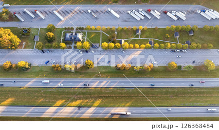 Big parking truck stop for tractor trailers rest area near busy American highway. Hauling cargo concept Big parking truck stop for tractor trailers rest area near busy American highway. Hauling cargo concept 126368484