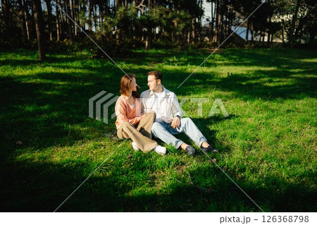 Couple enjoying a sunlit moment on a grassy patch in a serene park 126368798