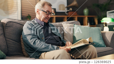 Senior man, reading book and relax on couch with study, literature and fiction in lounge at apartment. Elderly person, novel and knowledge on sofa with language, info or storytelling in living room 126369025