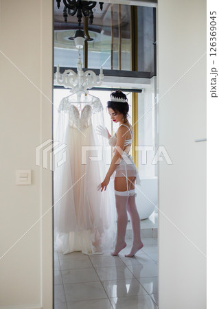 Seductive bride in a sexy lingerie and white stockings posing in a bathroom near her bridal dress 126369045