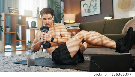 Fitness, laptop and man in home with weights for exercise, workout and training for muscle strength. Sports, living room and person with computer for online tutorial, video and streaming for wellness 126369377