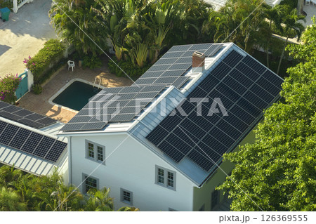 Aerial view of expensive american home roof with blue solar photovoltaic panels for producing clean ecological electric energy. Investing in renewable electricity for retirement income Aerial view of expensive american home roof with blue solar photovoltaic panels for producing clean ecological electric energy. Investing in renewable electricity for retirement income 126369555