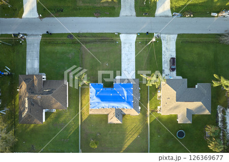 Aerial view of damaged in hurricane Ian house roof covered with blue protective tarp against rain water leaking until replacement of asphalt shingles 126369677