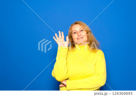 Middle age caucasian woman wearing a yellow sweater over blue isolated background waving hand with happy expression 126369893