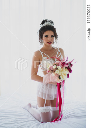 Seductive slender young bride in a sexy lingerie and white stockings posing on a bed with her bridal bouquet Seductive slender young bride in a sexy lingerie and white stockings posing on a bed with her bridal bouquet 126370021